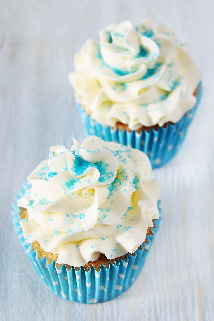 Two cupcakes topped with buttercream and blue sugar