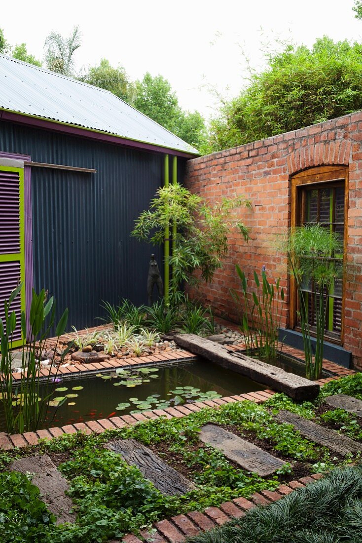 Landscaped pool and beds in courtyard with brick wall adjacent to house with corrugated metal cladding