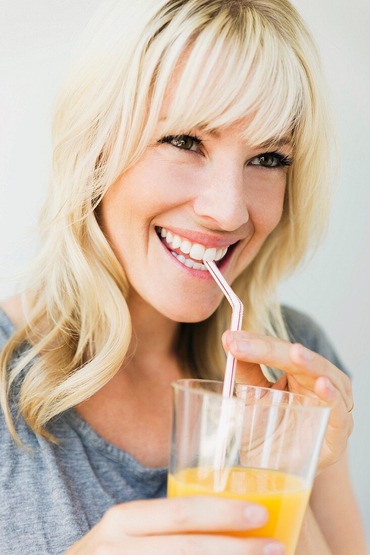 A blonde woman drinking orange juice through a straw