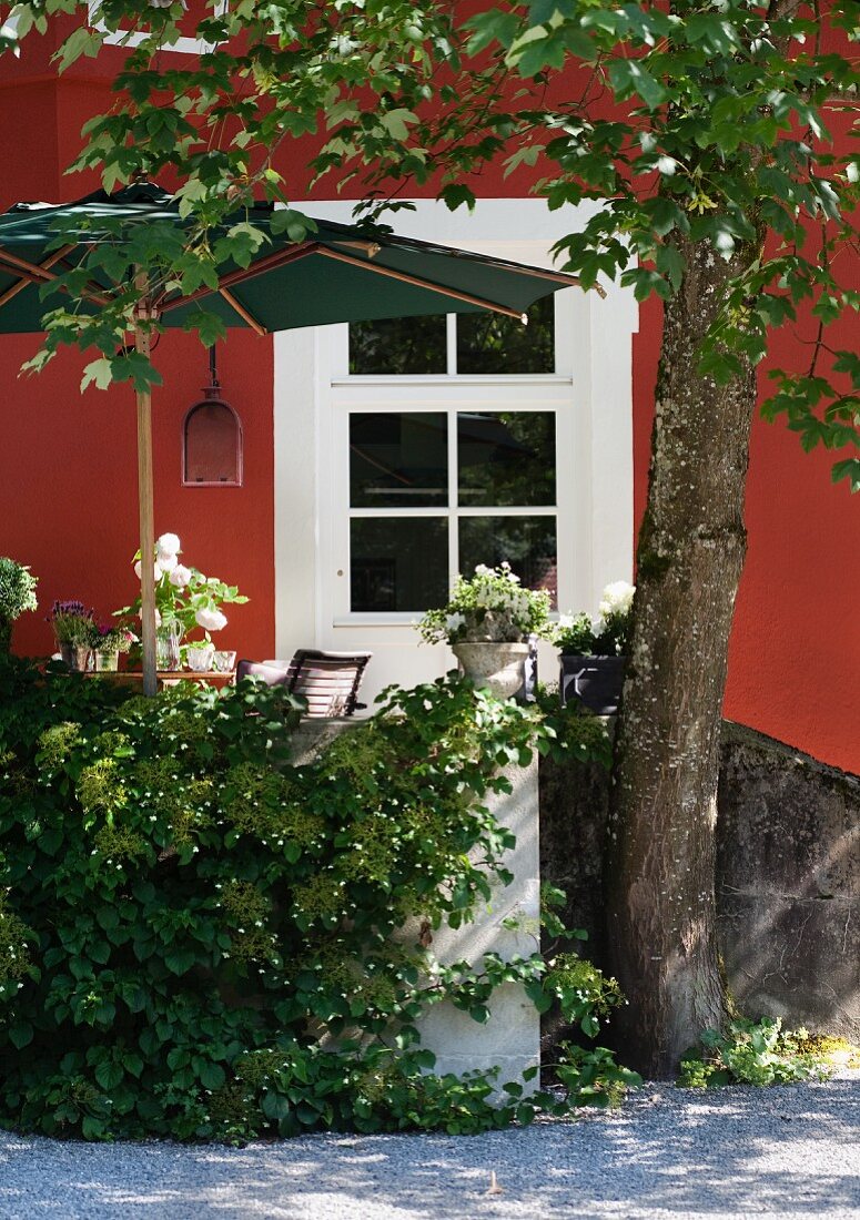 Sonniger Terrassenplatz mit Sonnenschirm eines renovierten Gutshauses mit roter Fassade und weißer Tür mit Fenstersprossen