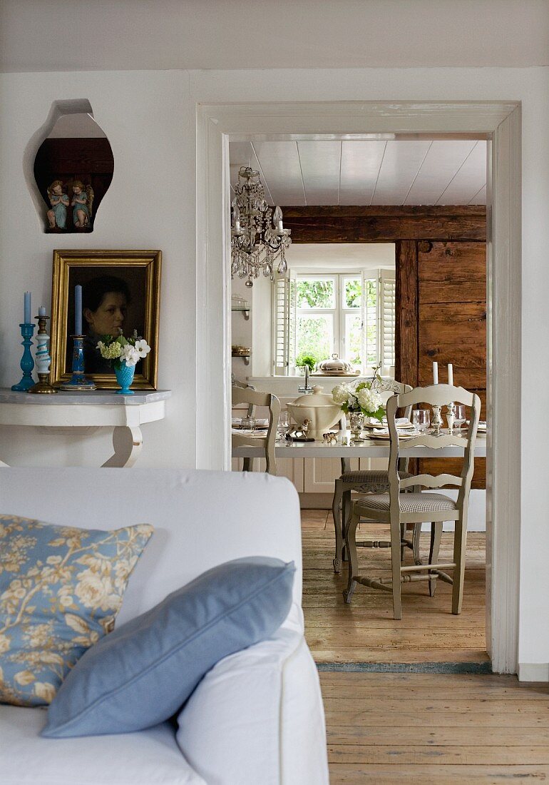 Partially visible couch with scatter cushions in front of doorway with view of festively set table in rustic dining room