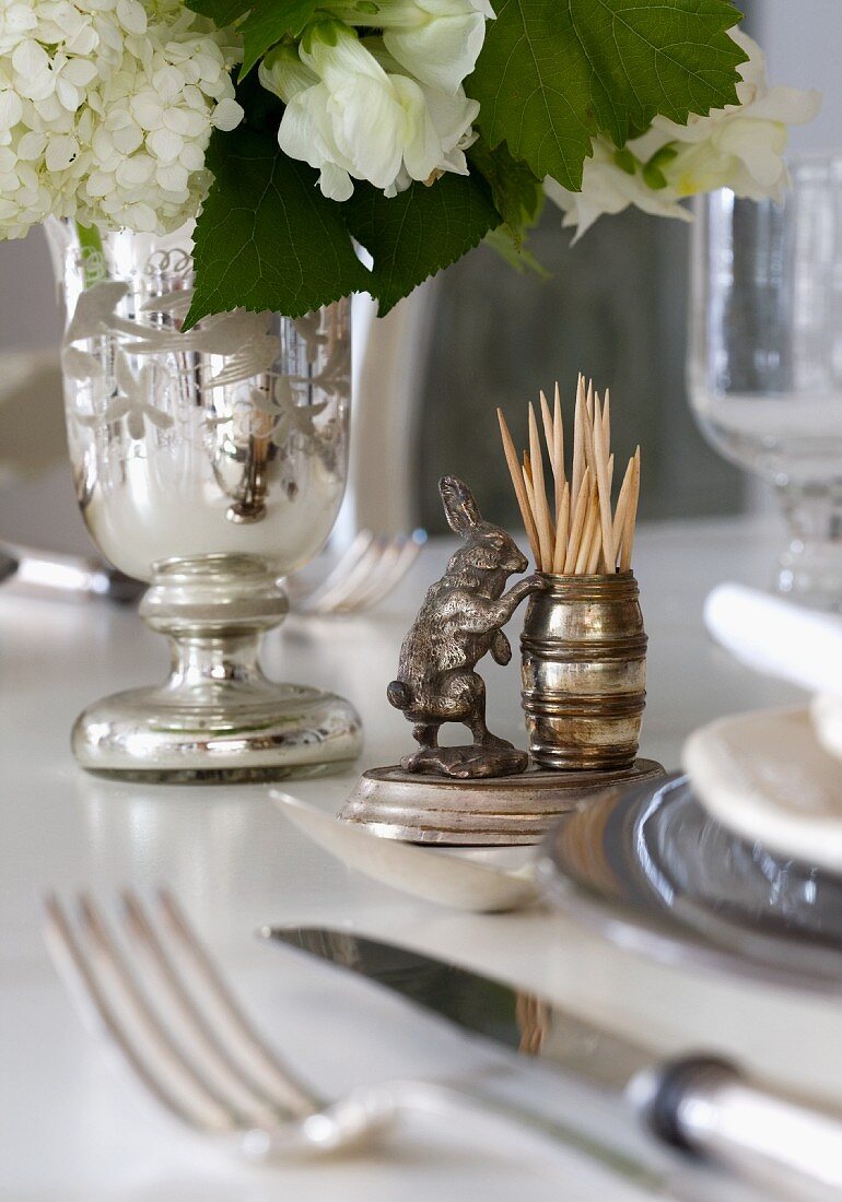 Zahnstocher Behälter mit Tierfigur aus Silber neben versilberter Vase mit weißem Gartenstrauss auf Tisch