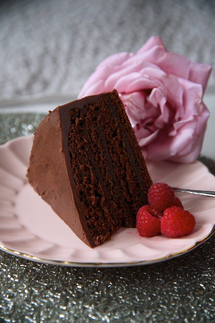 Ein Stück Schokoladentorte mit Himbeeren und Rosenblüte zum Valentinstag