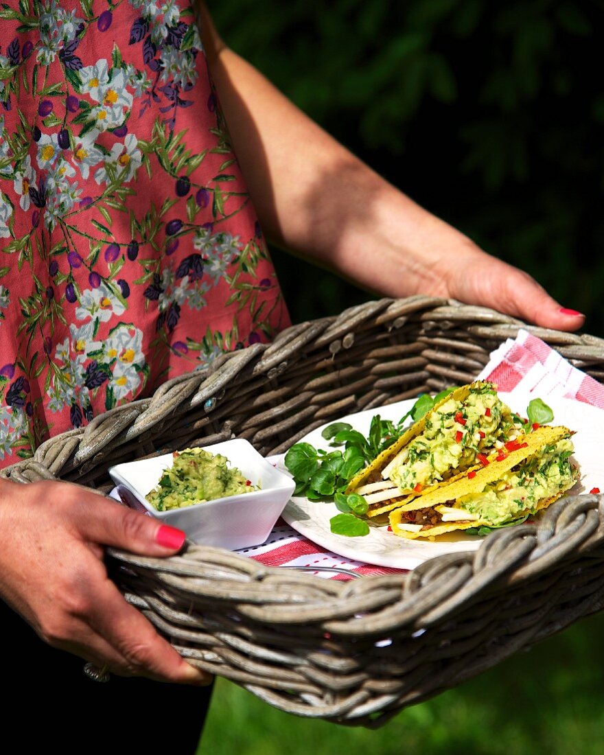 Frau hält Tablett mit Taco-Shells mit Guacamole