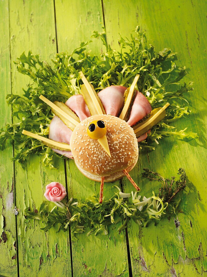 A peacock made from a sesame seed bun, ham, cheese and pickled gherkins