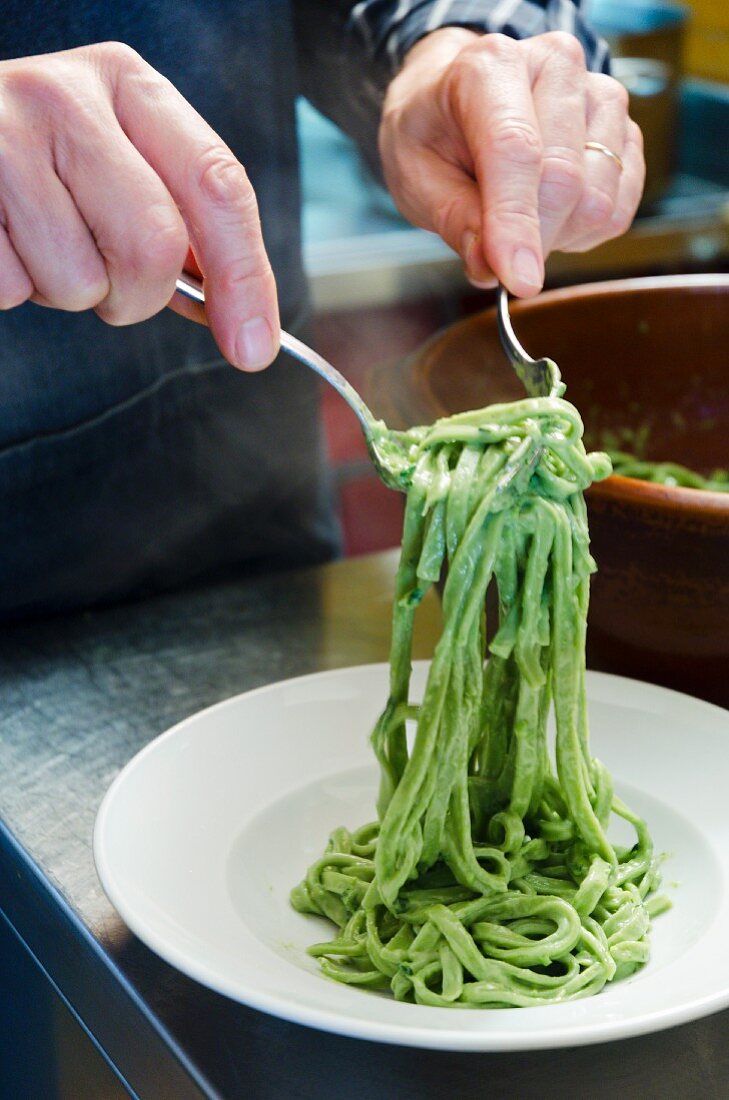 A man serving green tagliatelle