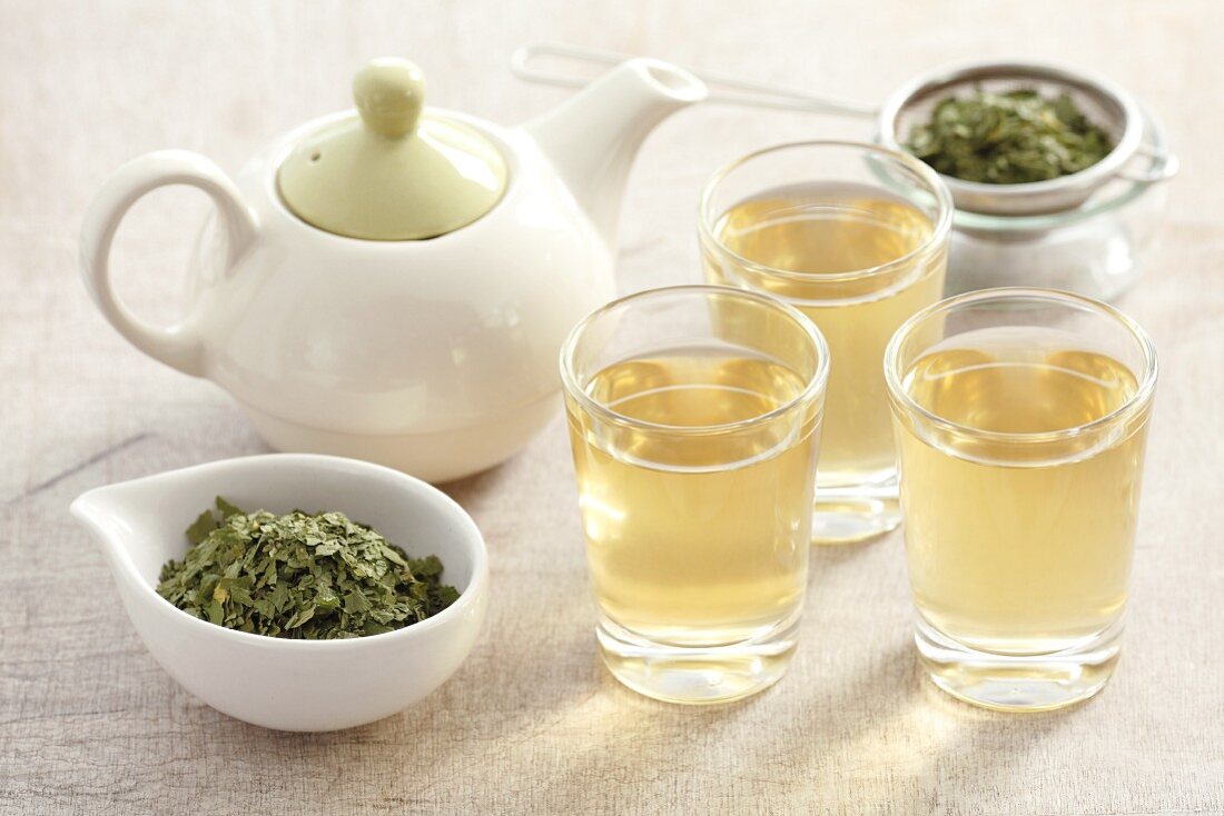 Three glasses of wild garlic tea, a teapot and tea leaves