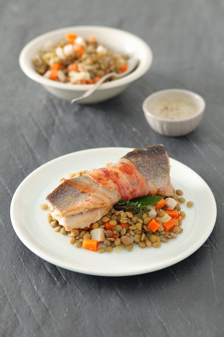 Trout wrapped in bacon on a lentil and carrot salad