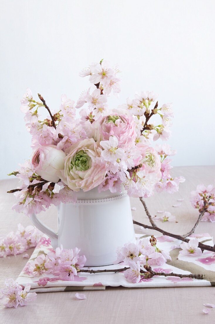 Frühlingsstrauss aus Ranunkeln und Zierkirschenblüten in Krugvase