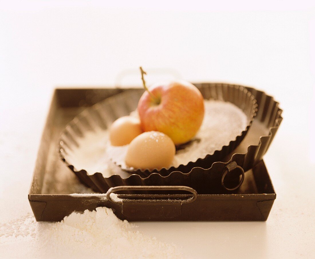 A still life featuring a baking tray, tart tins and baking ingredients