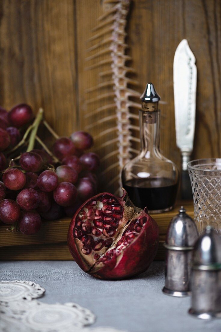 A still life featuring a fish skeleton, pomegranate, grapes and red wine