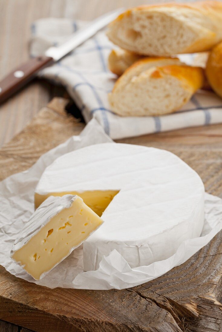 Camembert, one slice cut, on a wooden platter with chunks of baguette