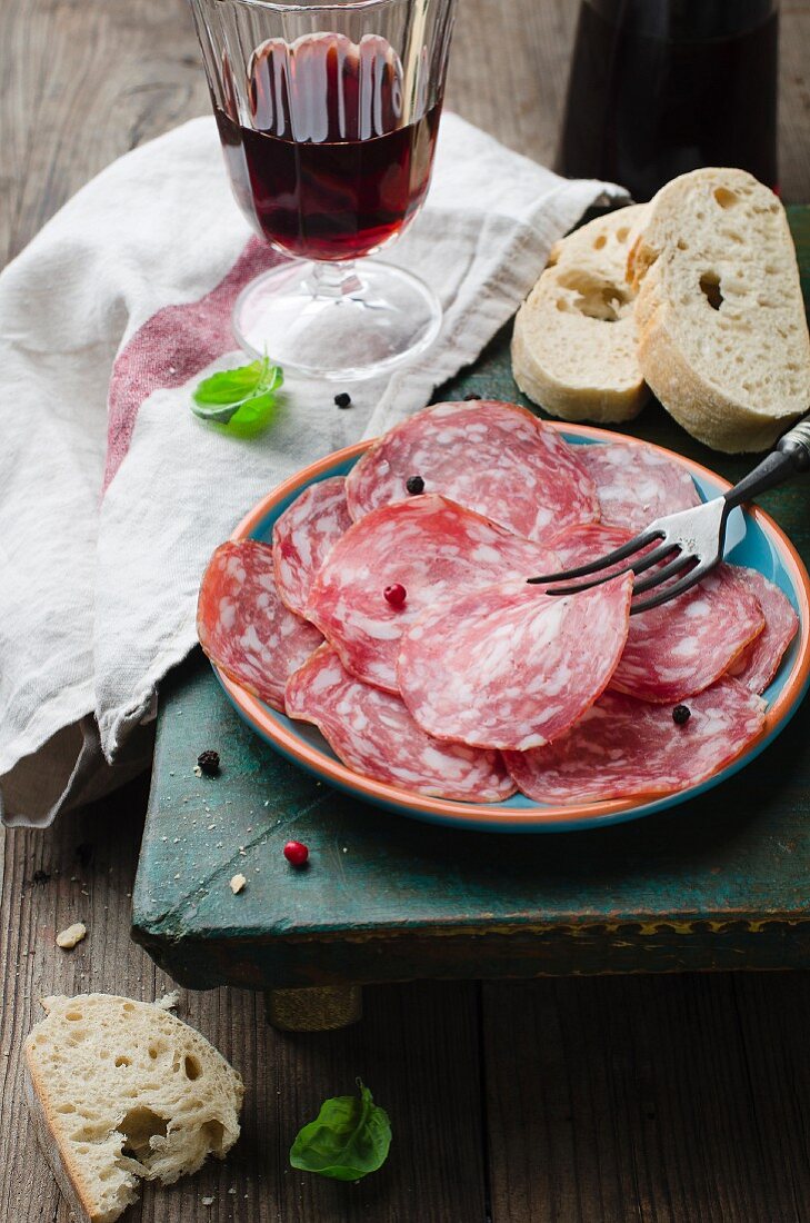 Thinly sliced salami, white bread and a glass of red wine