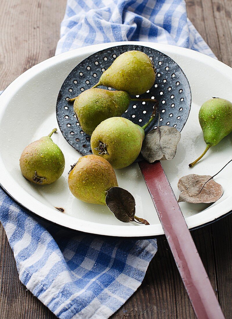 Several pears with water drops in a dish with a slotted spoon