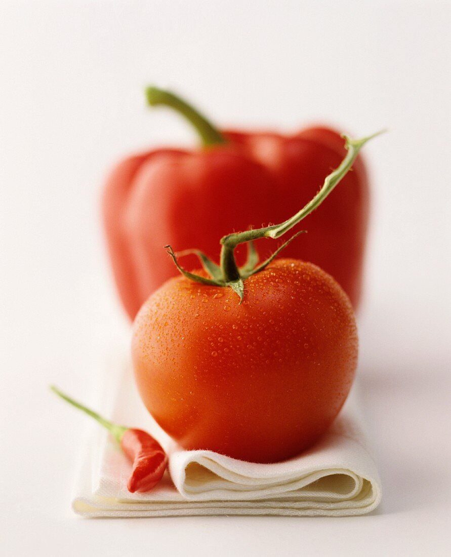 A still life featuring a red pepper, a tomato and a red chilli