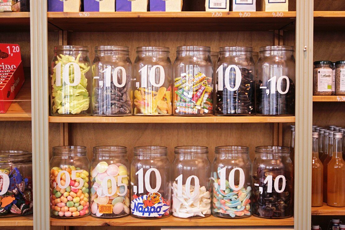 Verschiedene Süßigkeiten in offenen Schraubgläsern mit Stückpreis auf einem Holzregal