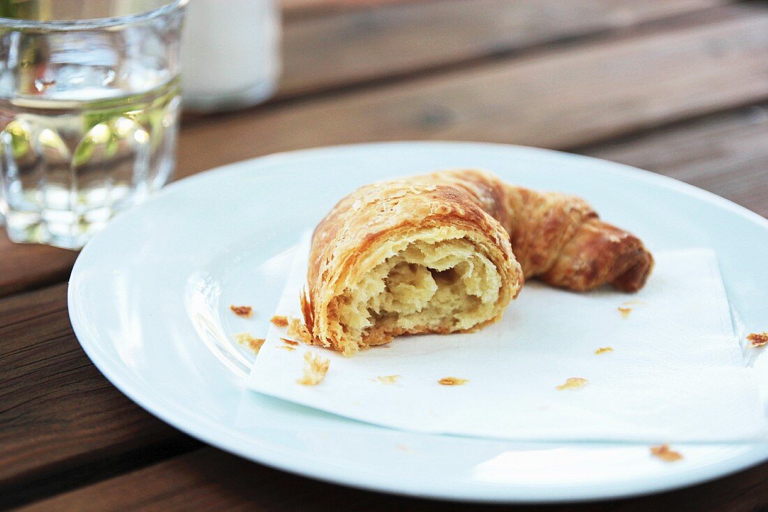 Part of a croissant on a plate with crumbs, in front of a glass of water