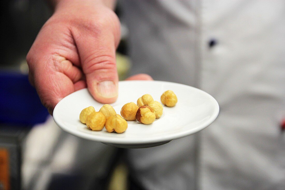 A pastry chef holding a small plate with a few Piedmont hazelnuts