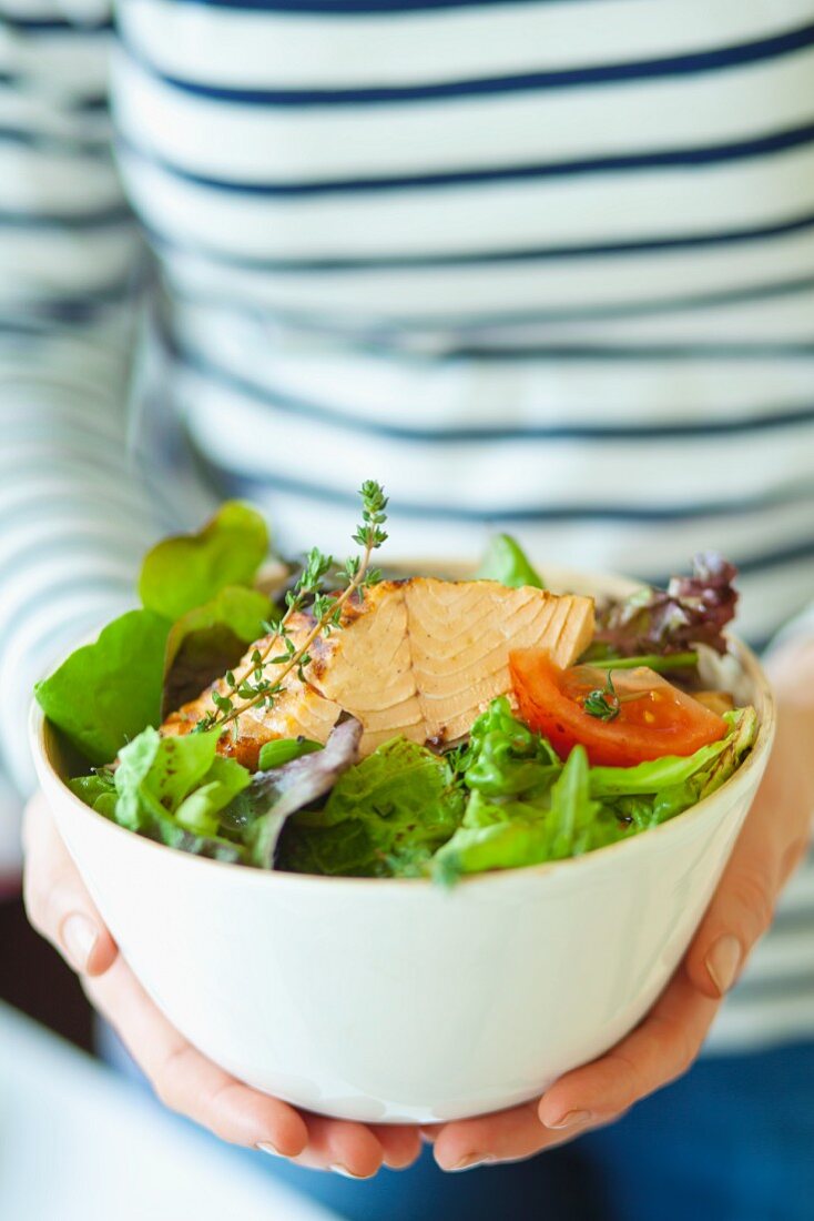 A woman holding a bowl of salad leaves with fried tuna, tomatoes and thyme