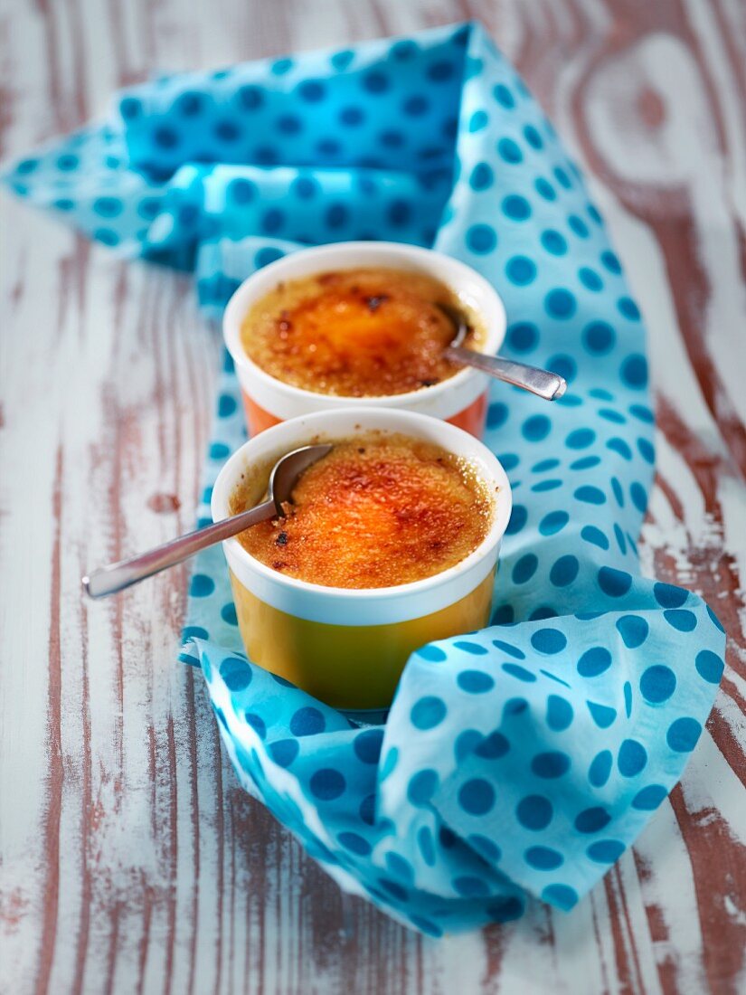 Zwei Schälchen Crème brûlée auf gepunktetem Tuch