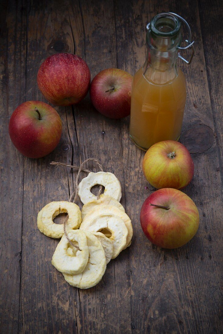 Frische Äpfel, Apfelsaft und getrocknete Apfelringe auf Holztisch