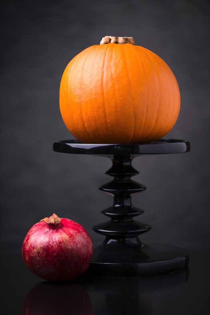 Orange squash on a cake stand with a pomegranate next to it