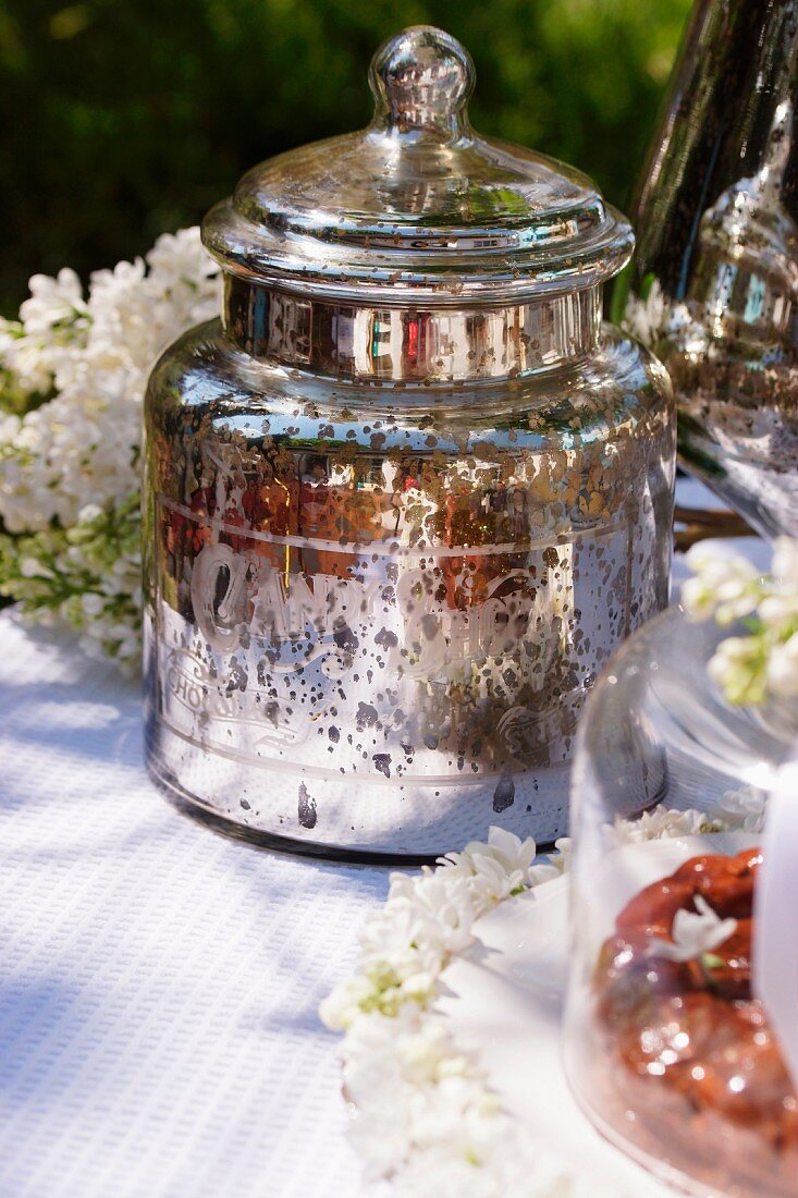 Silberdose, weisser Flieder und Kuchen auf Gartentisch