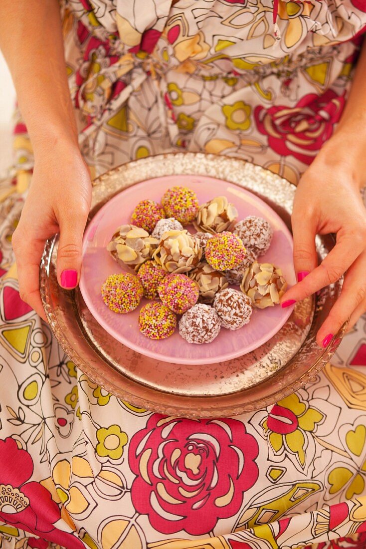 A woman holding a plate of chocolates coated with almonds, coconut and chocolate flakes
