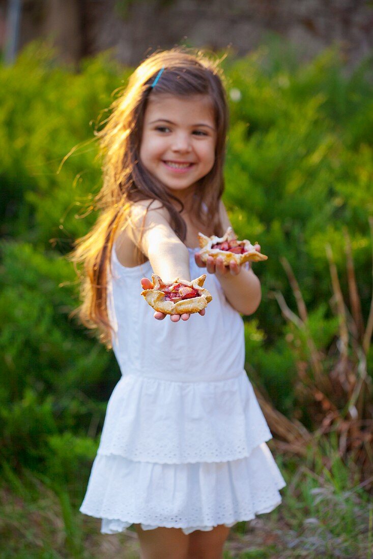Kleines Mädchen hält Rhabarbertorteletts im Garten