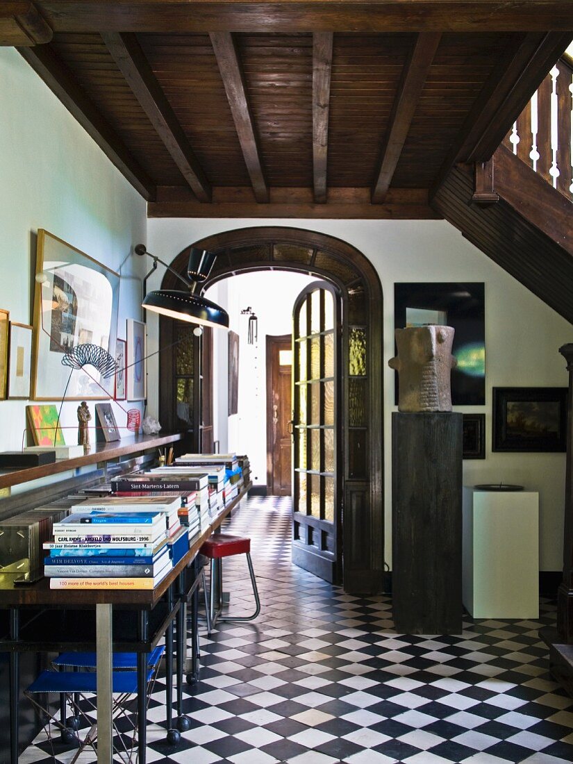 Vorraum mit schwarzweissem Schachbrettmusterboden, an der Seite Bücherstapel auf Konsolentisch unter Holz Galerie in Landhaus