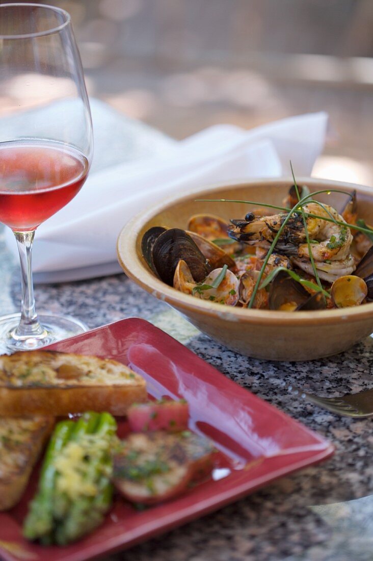 A Bowl of Seafood Stew with a Glass of Wine and a Plate of Toasted Bread