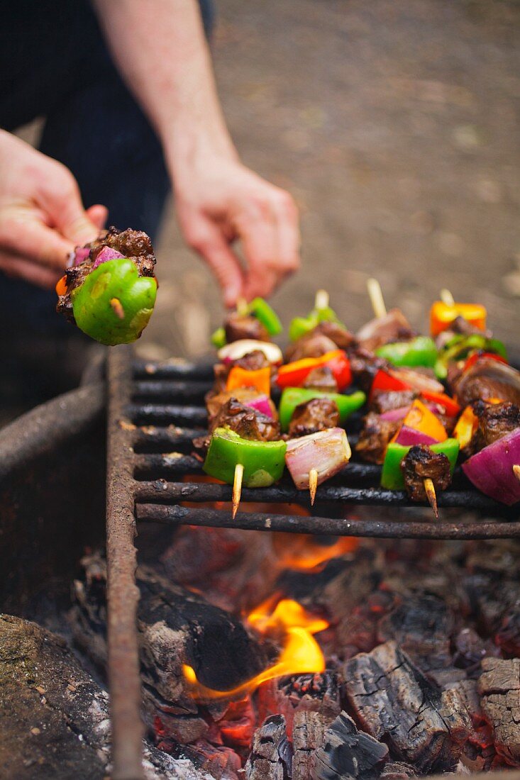 Mann grillt Fleischspiesse über Campingfeuer