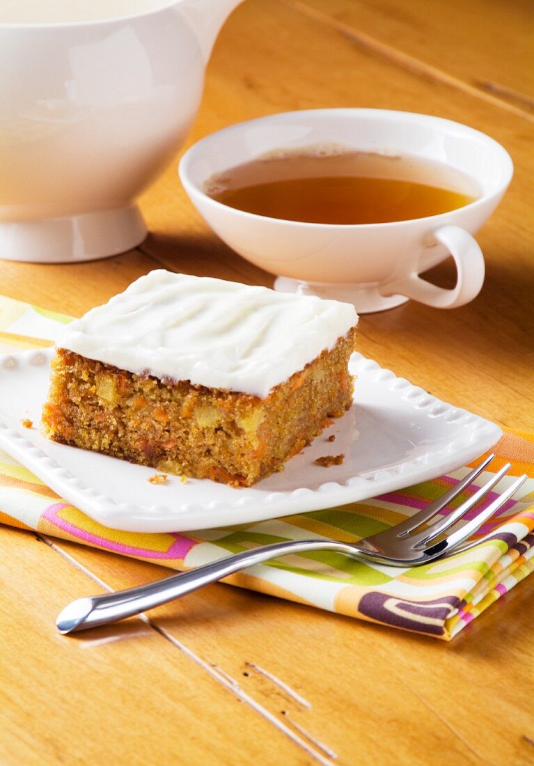 Ein Stück Karottenkuchen mit Glasur und eine Tasse Tee