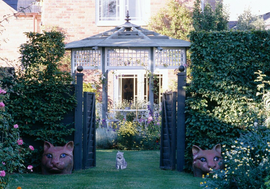 A cat and cat figures by the garden gate of an English country house with a summer house