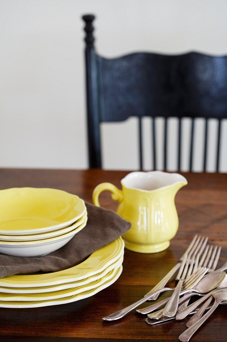 Gelbe Teller, Schälchen Milchkännchen und Besteck auf einem Holztisch