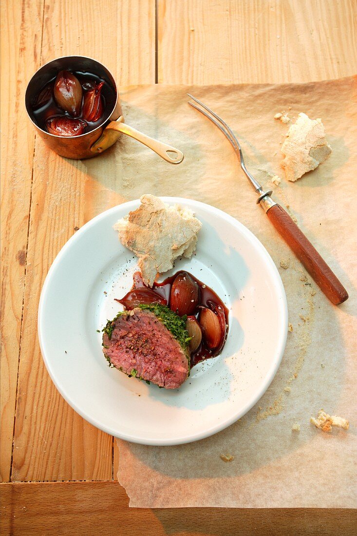 Beef fillet with a herb crust cooked in dough; served with shallots cooked in red wine