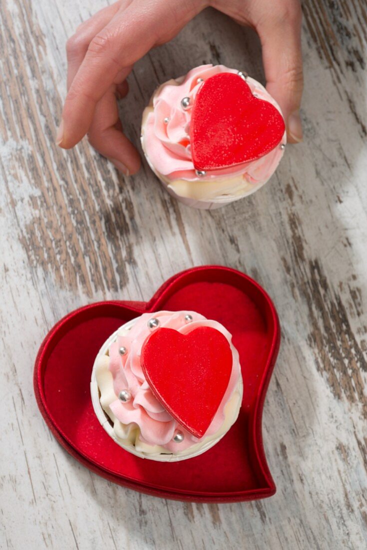 A hand reaching for a pink cupcake decorated with a red heart