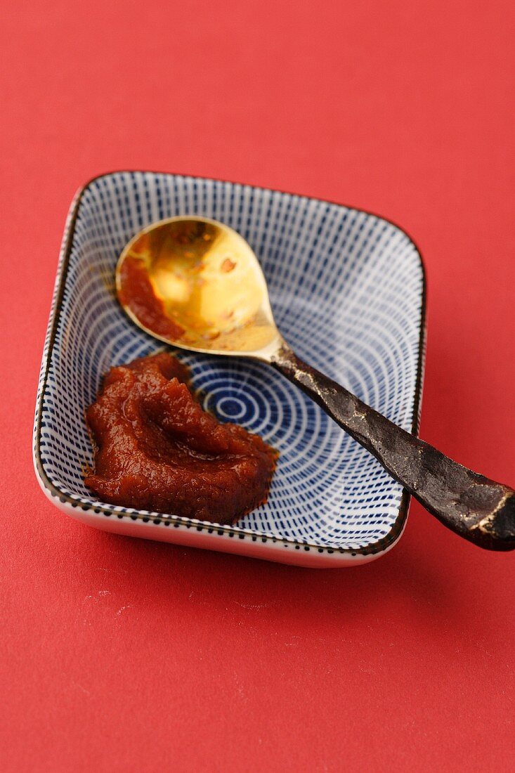 A spoon next to chilli paste in a blue bowl