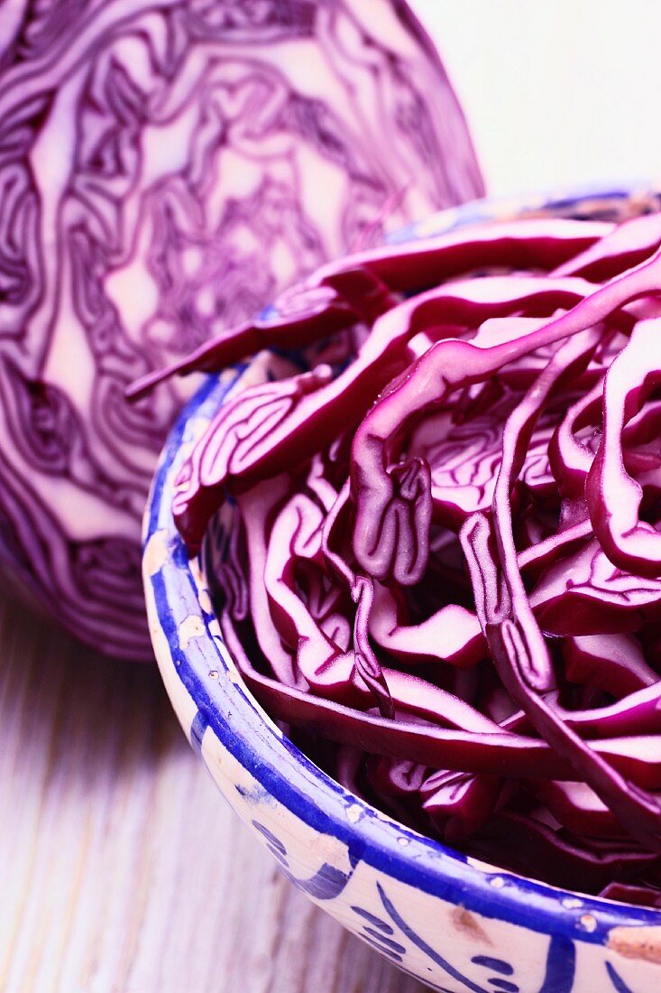 Sliced red cabbage in a bowl in front of half a red cabbage