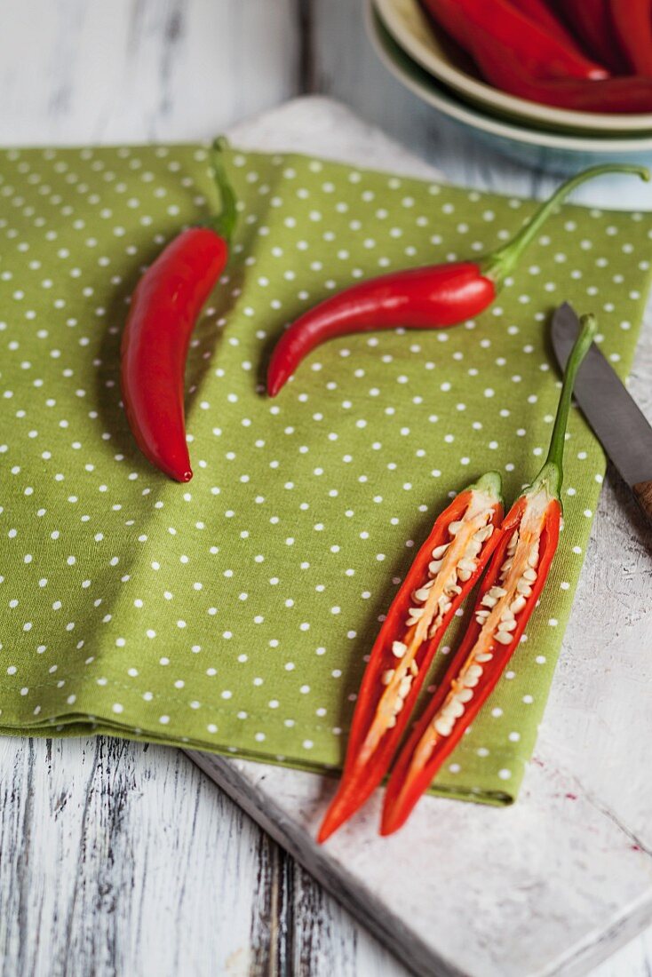 Aufgeschnittene Chilischoten auf Brettchen mit roten Peperoni in einer Schale