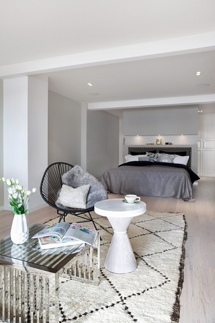 Shell chair with cord seat and modern side table on pale wool rug; elegant double bed in background