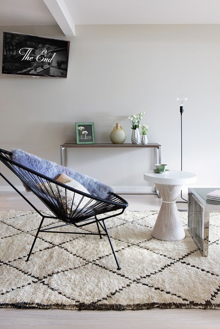 Shell chair with cord seat and side table on pale wool rug; vases on modern console table in background