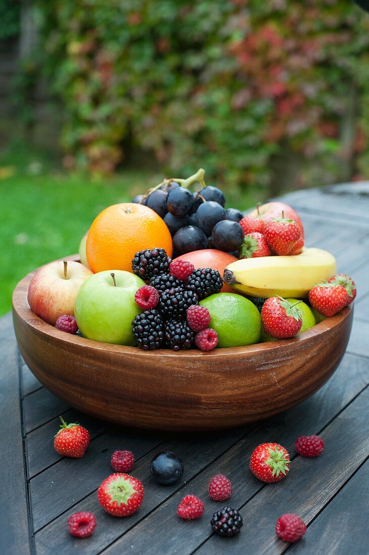 A large wooden bowl filled with fresh fruit and berries