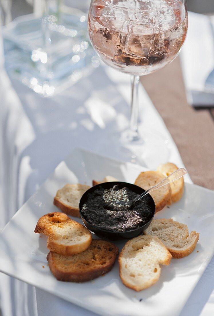 Tapenade, Röstbrot und Roseweinglas auf Gartentisch