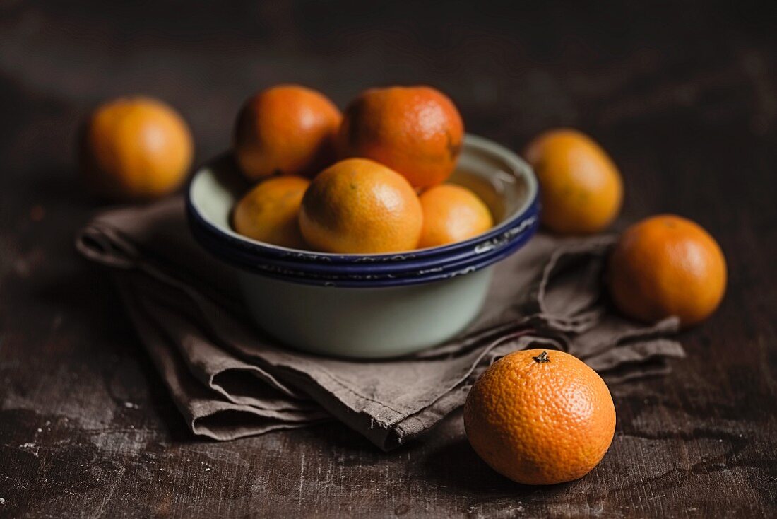 Clementines and enamel bowls on a wooden surface