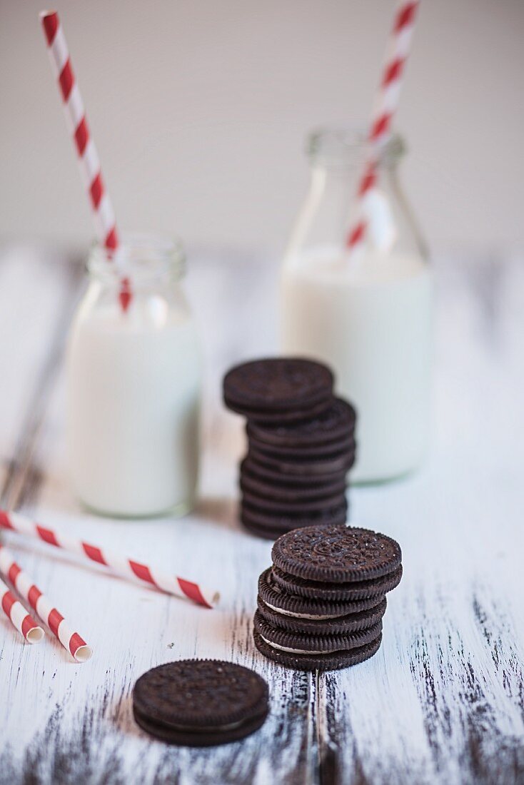 Stacks of Oreo cookies with bottles of milk and drinking straws on a wooden plate
