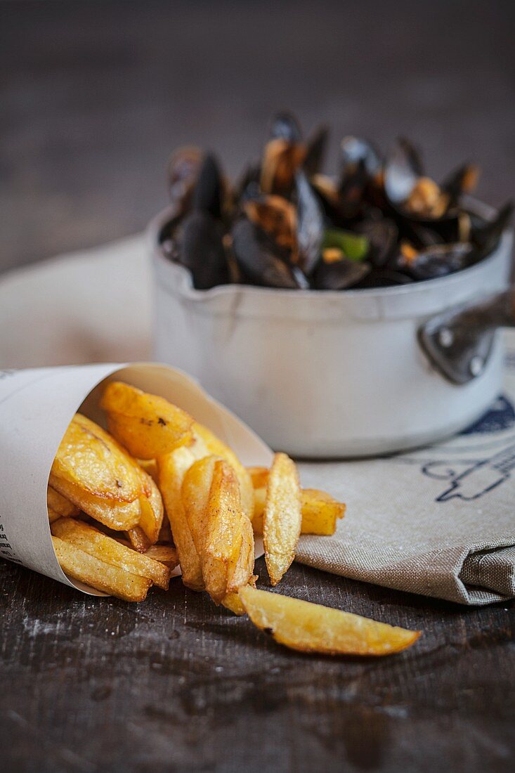 Steamed mussels in a saucepan and chips in a paper cone