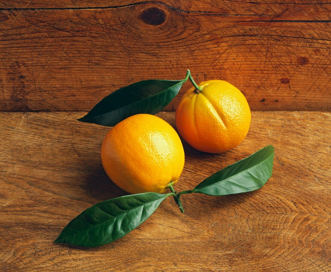 Zwei Orangen mit Blättern auf Holzuntergrund