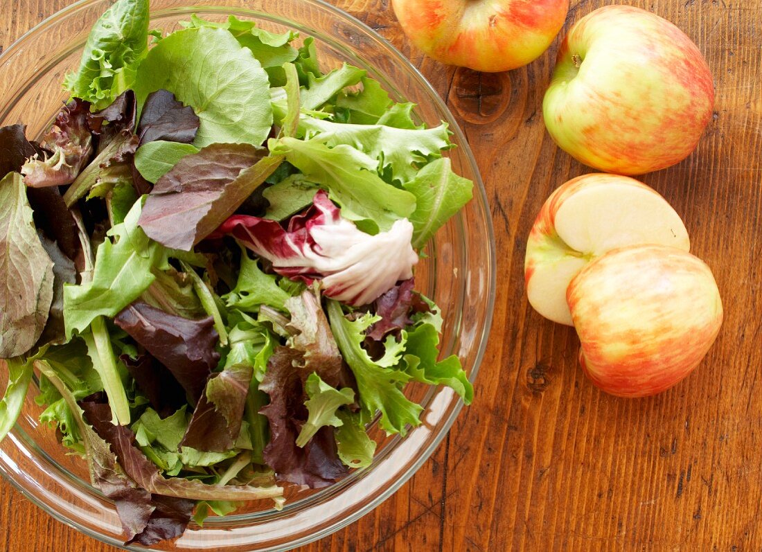 Gemischter Blattsalat in einer Schüssel, daneben Äpfel