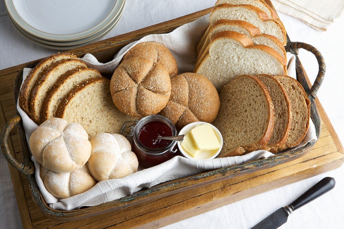 Korb mit Brotscheiben, Brötchen, Marmelade und Butter